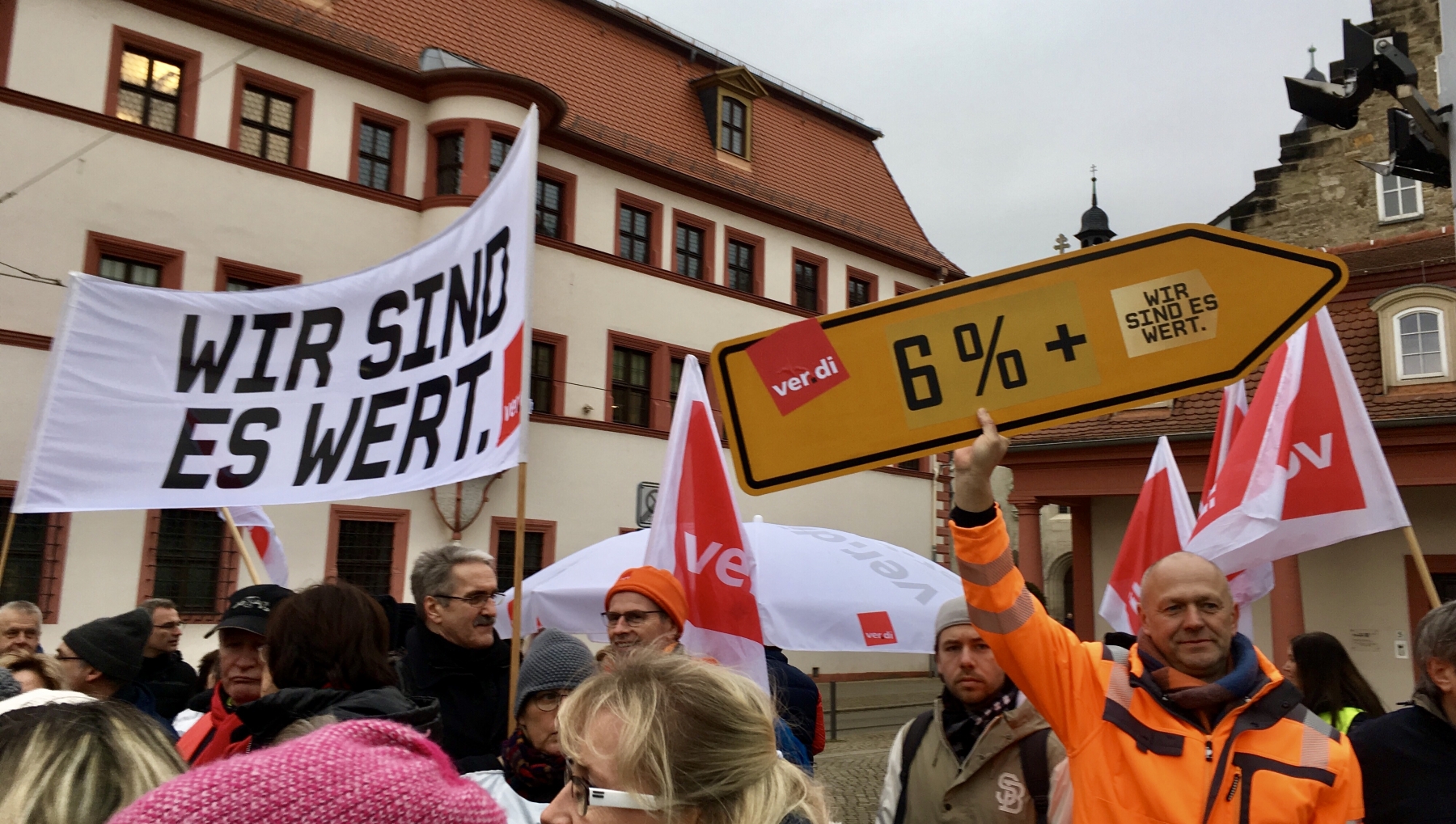 Demonstanten vor der Staatskanzlei. Mit einem Hochbanner "Wir sind es wert." ver.dei-Fahnane und einem Verkehrschild in For eines Wegweisers und mit der Aufschrift 6%
